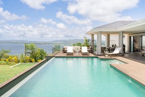Un espace piscine moderne avec des chaises longues, une terrasse en bois et une vue sur la mer.
