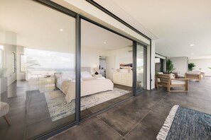 A modern hotel room with a large bed, a desk, and a view of the sea.