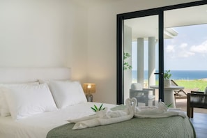 A hotel room with a bed, a nightstand, a lamp, a green throw, and a view of the ocean.
