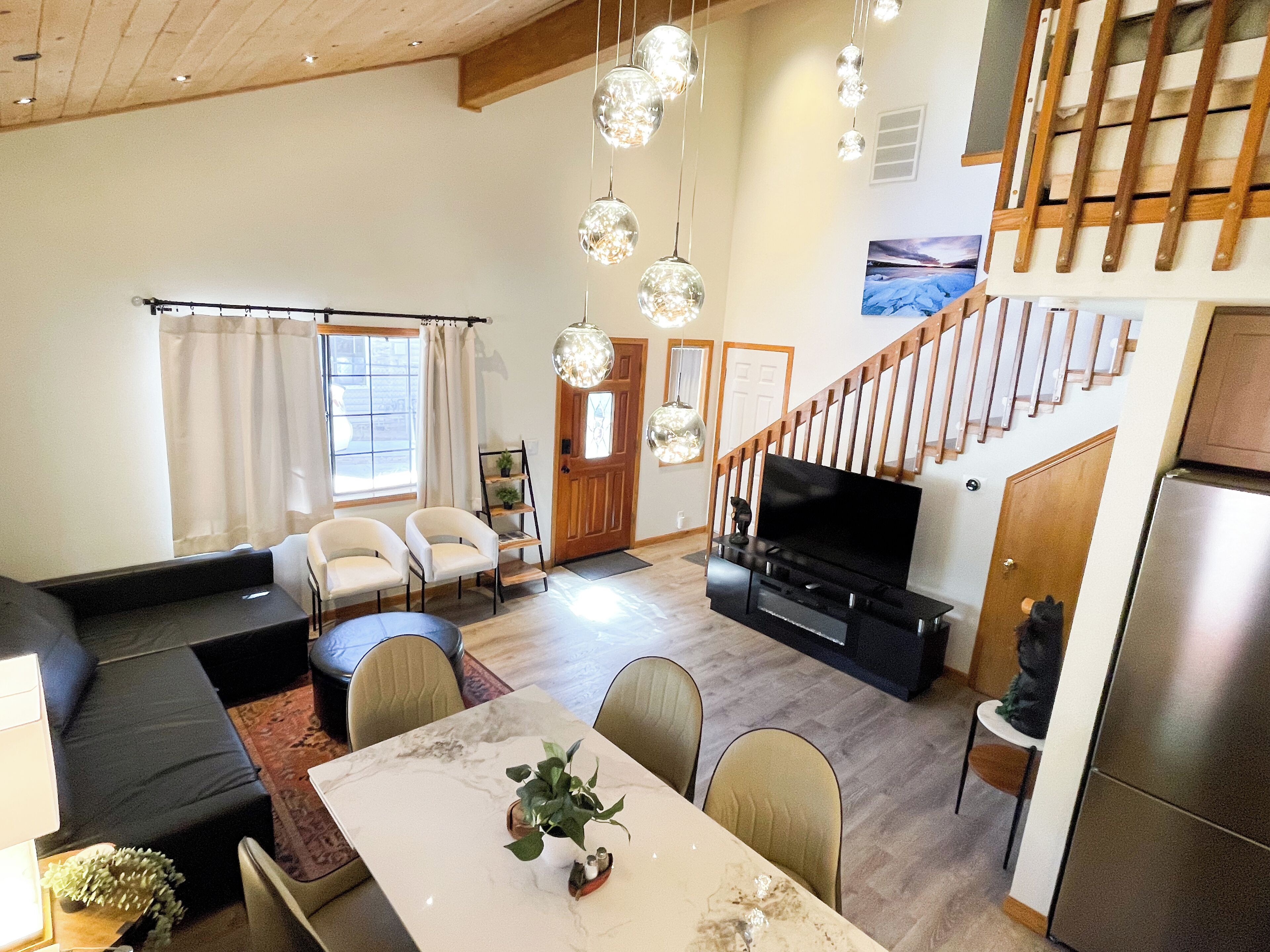 Een moderne woonkamer met een bank, stoelen, een eettafel en een televisie. Er is een trap die naar een ander niveau leidt.