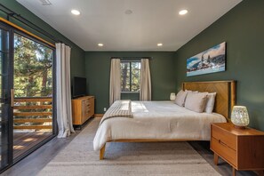 A bedroom with a large bed, a wooden nightstand, a TV, and a window with curtains. - Lakefront Modern Cabin w/ Game Room, Fire Pit! (Big Bear Lake)