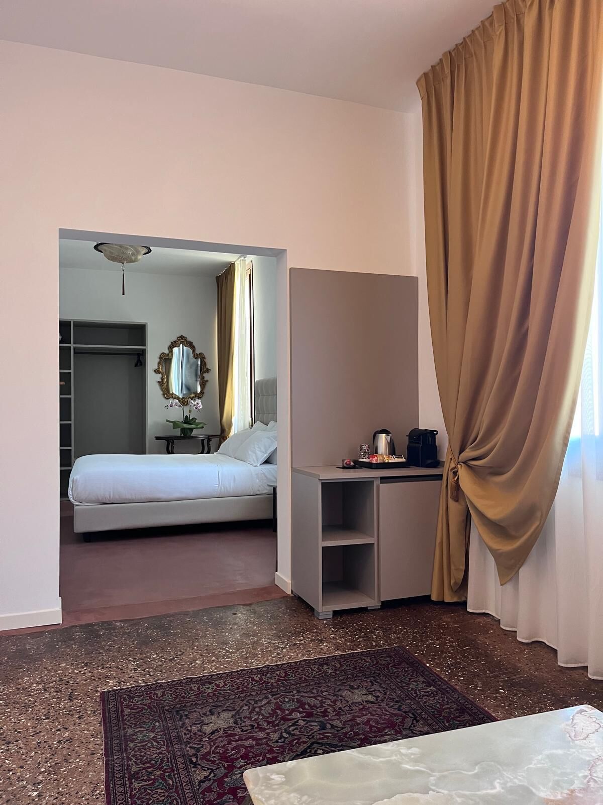 A hotel room with a bed, desk, and a view through an open door.