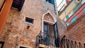A narrow alleyway with a brick building featuring a small balcony with a metal railing. - Casanova Hideaway (Venice)