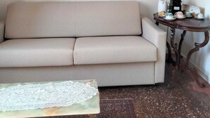A living room with a beige sofa, a small round table with a coffee maker, and a decorative wall piece. - Casanova Hideaway (Venice)