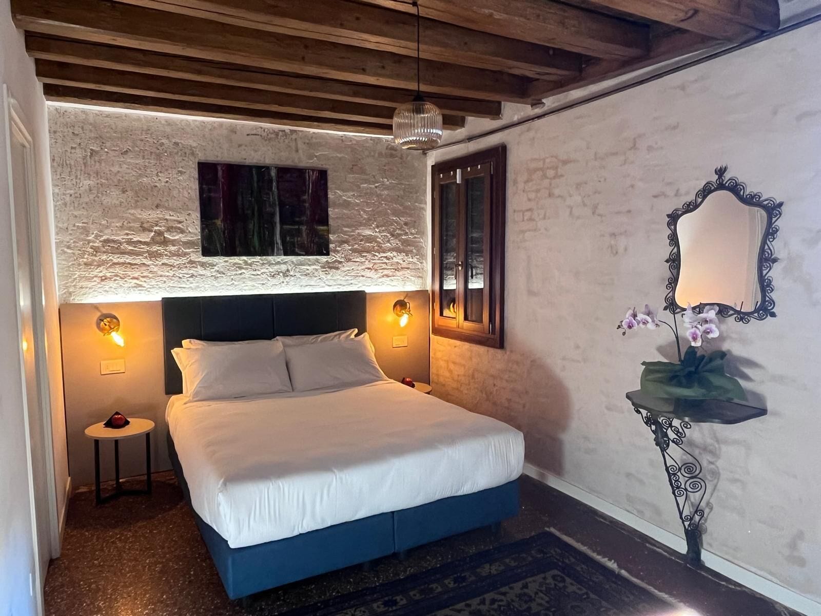 A bedroom with a bed, a nightstand, a wall-mounted mirror, and a decorative plant.
