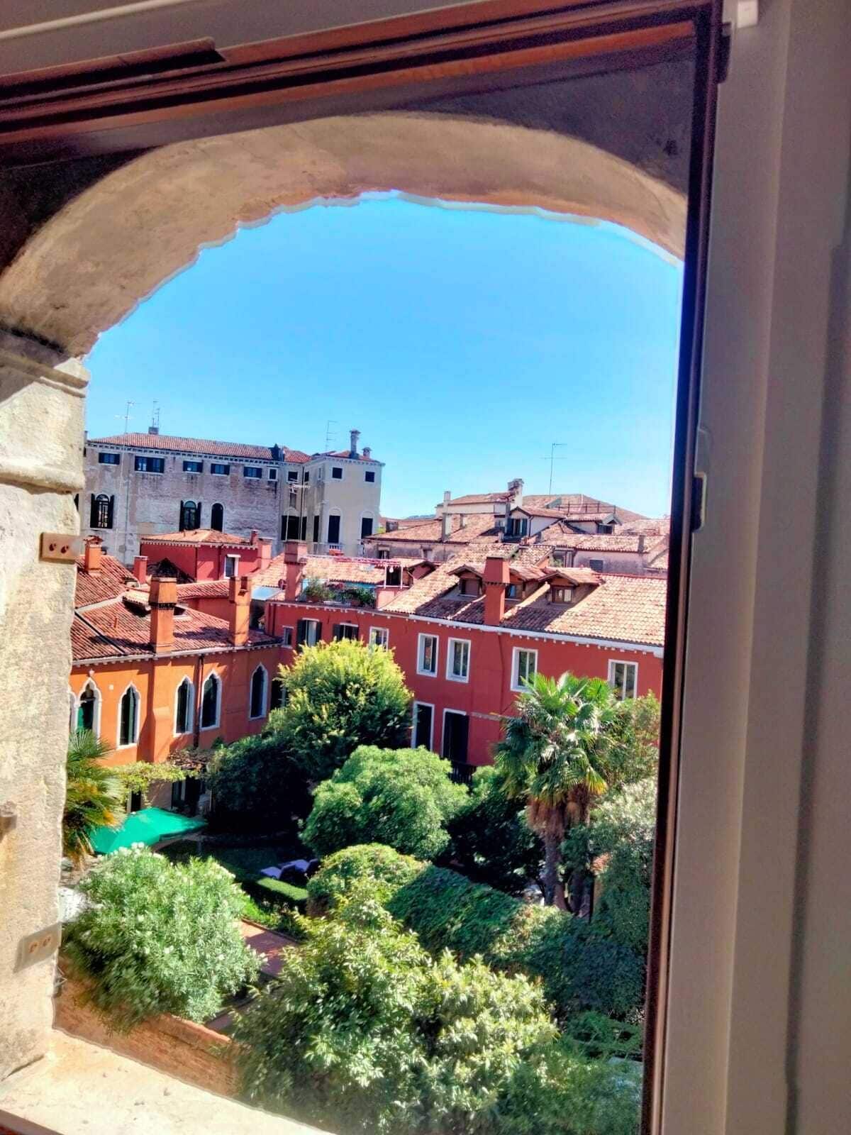 Une vue sur une cour intérieure, à travers une arche, avec des bâtiments et de la verdure.