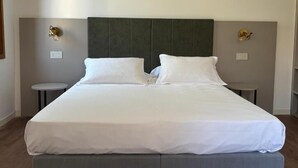 A large bed with a grey headboard, two bedside tables, and wall-mounted lamps. - Casanova Hideaway (Venice)