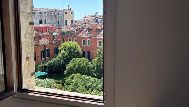 A view through a window with an arch, displaying a courtyard with buildings and greenery. - Casanova Hideaway (Venice)