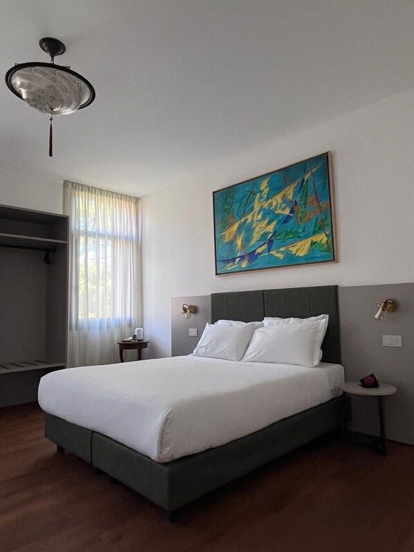 A hotel room with a large bed, a ceiling fan, a window with curtains, and a painting on the wall. - Casanova Hideaway (Venice)