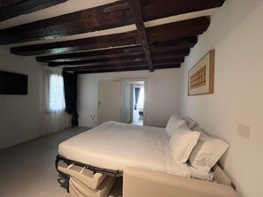 A bedroom with a bed, a wardrobe, a door leading to another room, and a window with curtains. - Casanova Hideaway (Venice)