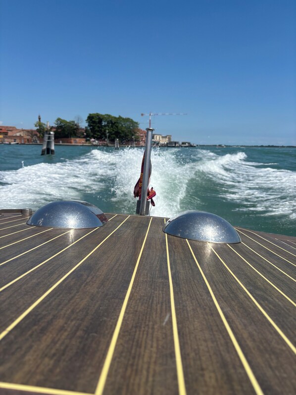 A boat's deck with a wake, a mast, and a cityscape in the background. - Casanova Hideaway (Venice)