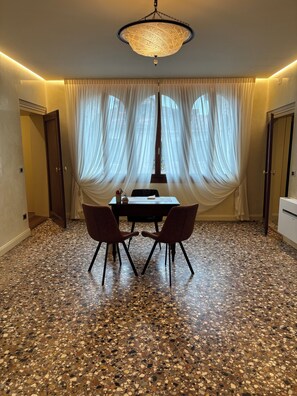 A dining area with a table and chairs, a chandelier, and a floor with a speckled pattern. - Casanova Hideaway (Venice)