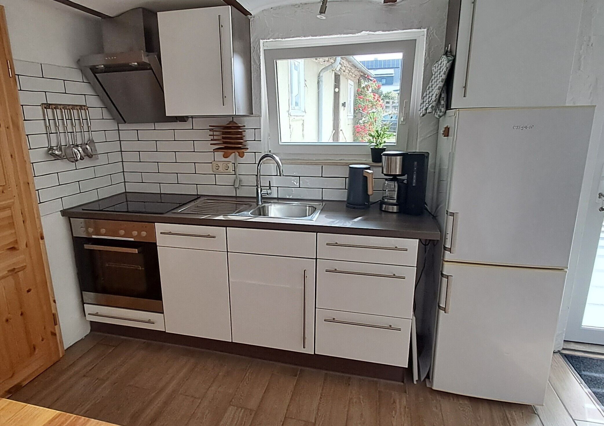 Eine Küche mit weißen Schränken, einer Edelstahl-Spüle, einem Einbauofen und einem Kühlschrank.