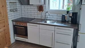 A kitchen with white cabinets, a black stove, a sink, and a coffee maker. - Vacation apartment in country house style. small, cozy and quiet location (Wasserlosen)