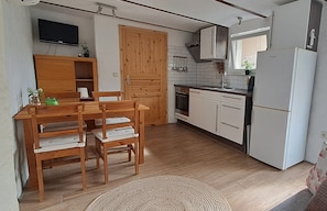 Eine kleine Küche mit Holztisch und -stühlen, einem eingebauten Ofen, weißen Schränken und einem weißen Kühlschrank.