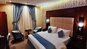 A hotel room with a large bed, a small round table, two chairs, and a TV. - Neroz Inn Furnished Apartments (Jeddah)