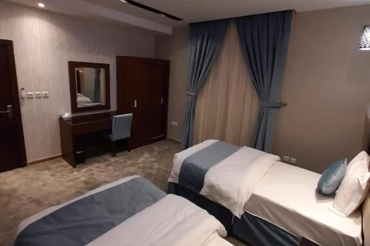 A hotel room with two beds, a desk, a chair, and a large window with curtains.