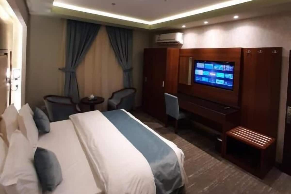 A hotel room with a bed, a desk with a computer, a TV, and an air conditioning unit.