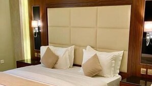 A hotel room with a large bed, a wooden headboard, a bedside table, a chair, and a small round table. - Neroz Inn Furnished Apartments (Jeddah)