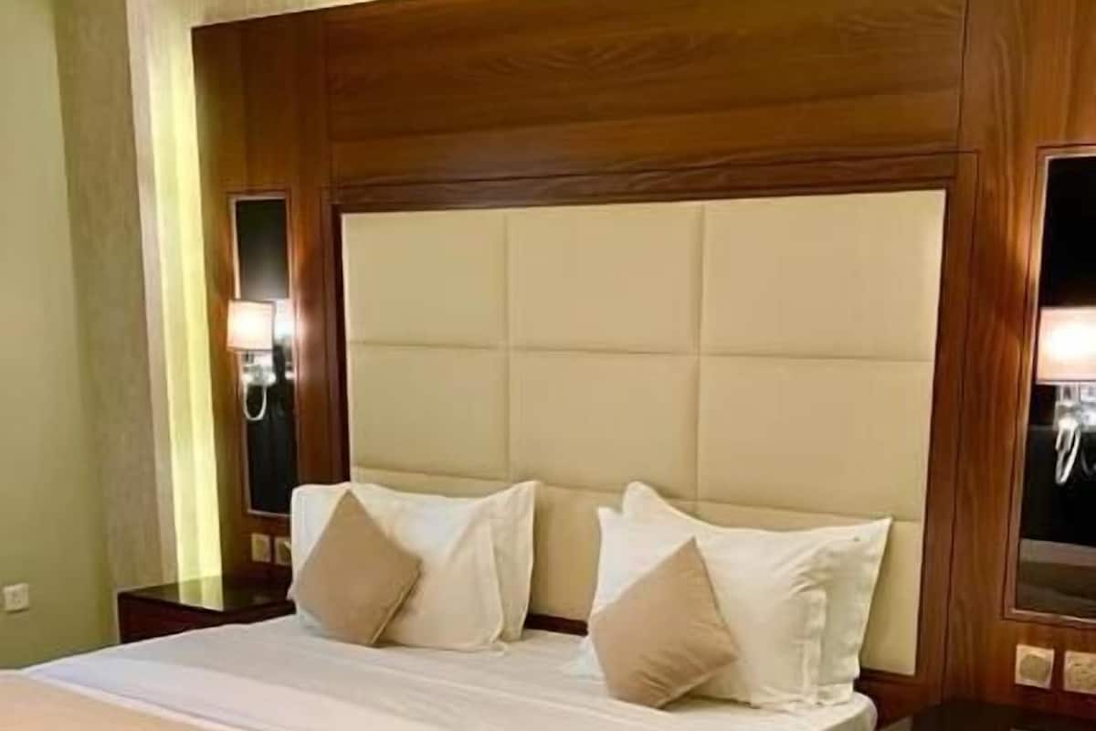 A hotel room with a large bed, a wooden headboard, a bedside table, a chair, and a small round table.