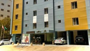 A multi-story hotel with a modern design, featuring a mix of yellow and grey facades, multiple windows, and a visible entrance with a car parked in front. - Neroz Inn Furnished Apartments (Jeddah)