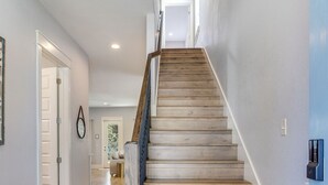 Un escalier avec des marches en bois et une rampe métallique, menant à un palier doté d’une porte.