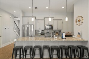 Una cocina moderna con encimeras de granito, electrodomésticos de acero inoxidable y taburetes de bar negros.