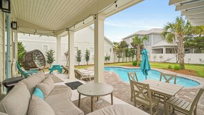 Une terrasse couverte avec une piscine, du mobilier d’extérieur et une chaise suspendue.