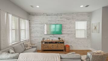 A living room with a grey sofa, a wooden TV stand, and a large flat-screen TV mounted on a white brick wall.