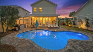 Une maison à deux étages avec une piscine, un patio couvert et une cour arrière bien éclairée.