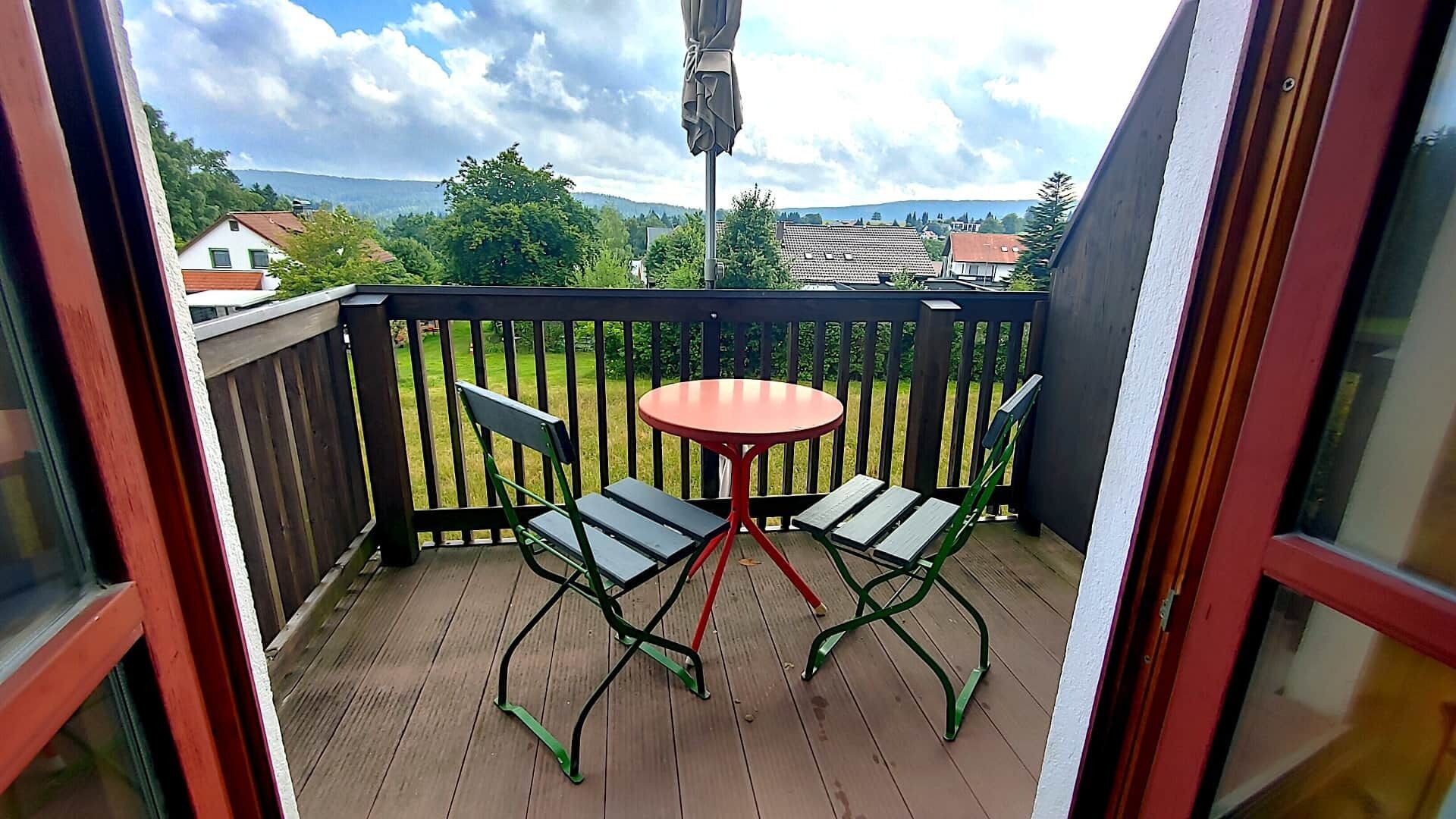 Ein Balkon mit Holzdeck, einem runden Tisch und zwei Stühlen.