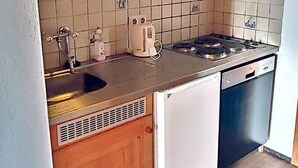 Una cocina compacta con armarios de madera, salpicadero de azulejos, estufa, fregadero y lavavajillas integrado.