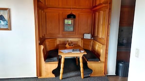 Un rincón acogedor con un banco y una mesa de madera, una ventana pequeña y un cubo de basura.