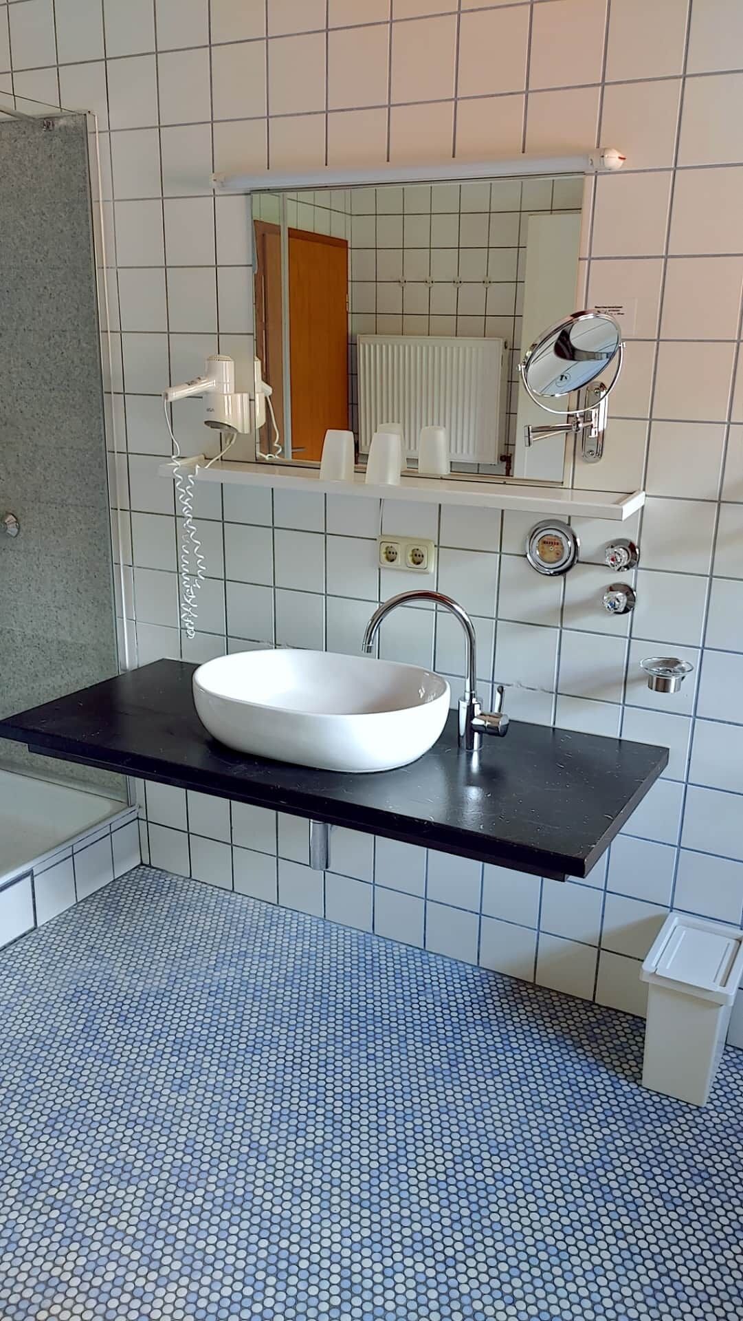 Une salle de bain moderne avec un lavabo blanc, un plan de toilette noir et un sol carrelé.
