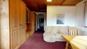 A wooden interior with a sofa and a table, a hallway leading to a bathroom, and a painting on the wall. - Holiday apartment "Rudolphstein" – 2-4 Guests (Warmensteinach)