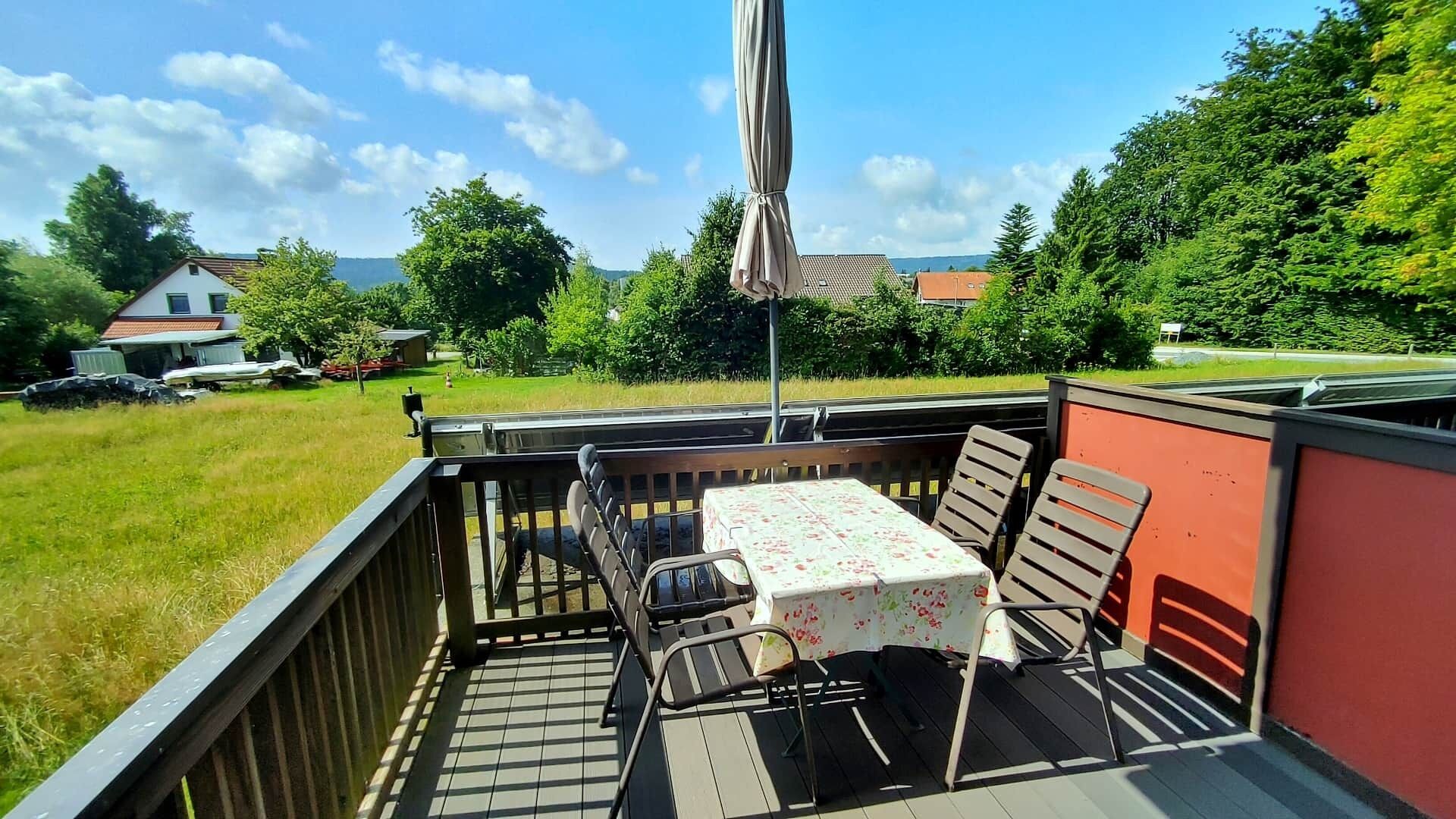 A balcony with a table and chairs, a view of a grassy field, and a red wall.