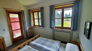 Ein Zimmer mit zwei Betten, einem Sessel, einem Fernseher und großen Fenstern mit Vorhängen.