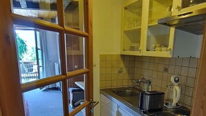 Eine Küche mit Holztür, weißen Schränken, einem Spülbecken, einem Herd und einer Pendelleuchte.