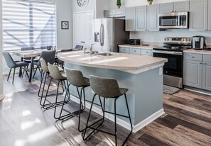 A modern kitchen with a central island, bar stools, stainless steel appliances, and a dining area with chairs.