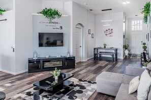 A modern living room with a flat-screen TV, black entertainment unit, grey sofa, and a patterned rug.