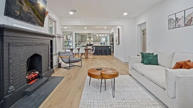 A modern living room with a fireplace, a white sofa, and a dining area in the background. - Stylish Bungalow. Sleeps 6. Wi-fi. Pets welcome. (Oklahoma City)