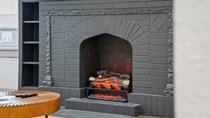 A modern outdoor fireplace with a brick design, a fire burning inside, and a wooden bench nearby. - Stylish Bungalow. Sleeps 6. Wi-fi. Pets welcome. (Oklahoma City)