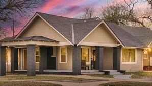 A two-story house with a gabled roof, a front porch, and a garage. - Stylish Bungalow. Sleeps 6. Wi-fi. Pets welcome. (Oklahoma City)