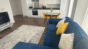A modern living room with a blue sofa, a TV, and a kitchen in the background. - London Luxe Apartment With 3 Bedrooms (London)