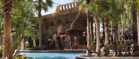 Un'area piscina con un grande edificio caratterizzato da finestre ad arco e un cartello con la scritta 'TRIBULATION'.