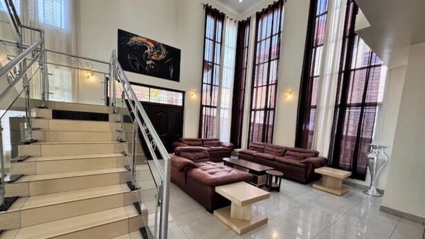 A spacious living area with a staircase, leather sofas, and a large window with curtains. - Mu Rugo by Iwacu Stays (Kigali)