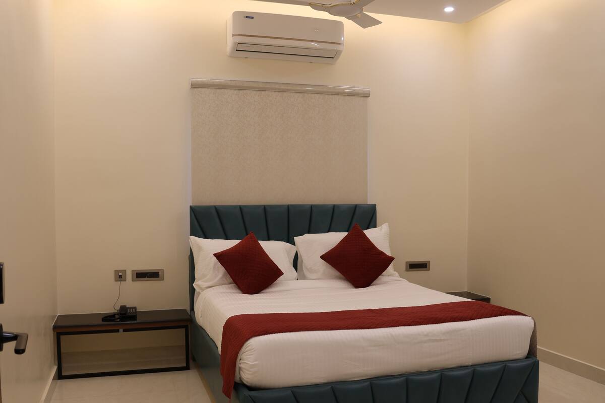 A modern hotel room with a large bed, a bedside table, an air conditioning unit, and a nightstand.