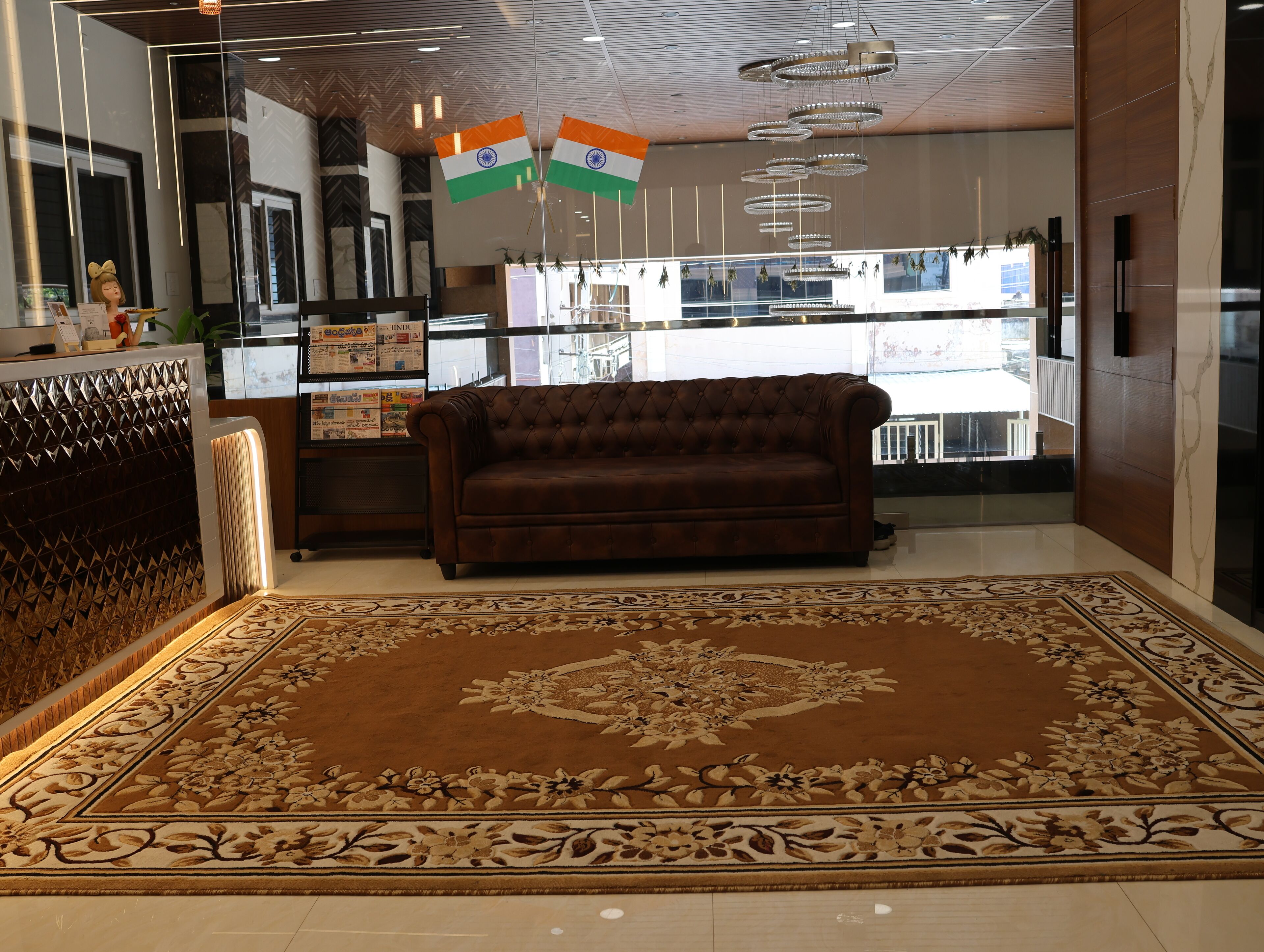 Eine Lobby mit einem braunen Sofa, einem gemusterten Teppich und zwei indischen Flaggen.