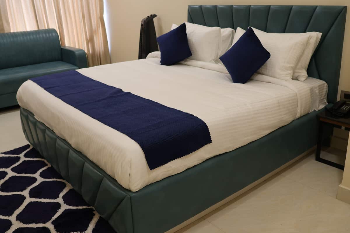 A neatly made bed with a green headboard, white and navy blue bedding, and a matching green sofa in the background.