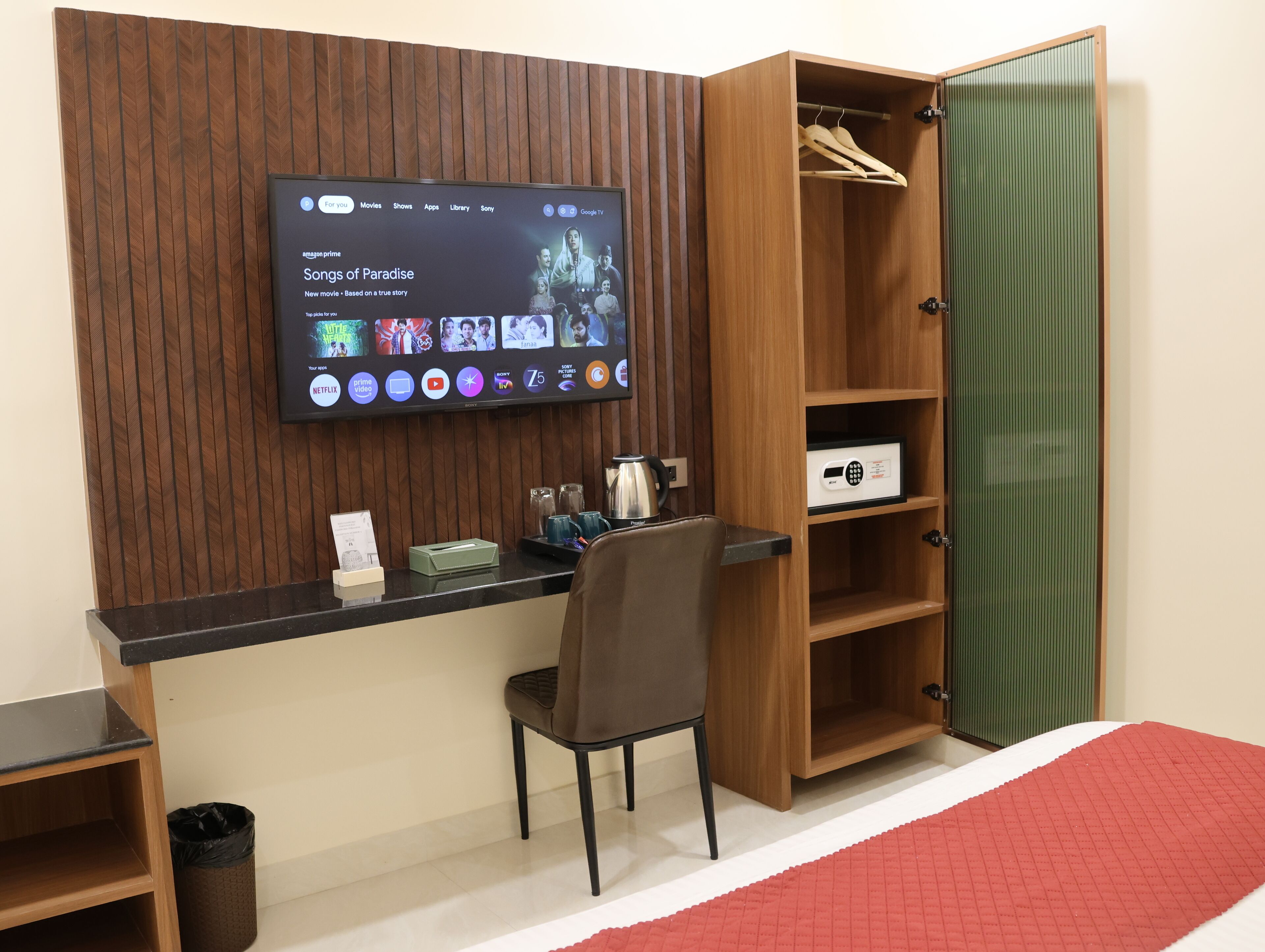 Une chambre d’hôtel avec un bureau en bois, un téléviseur fixé au mur, un rideau vert et un tapis rouge.